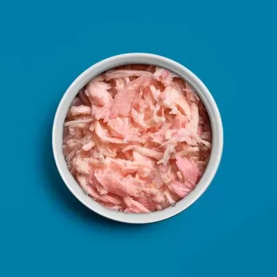 Tigela branca com frango desfiado rosa clara sobre fundo azul