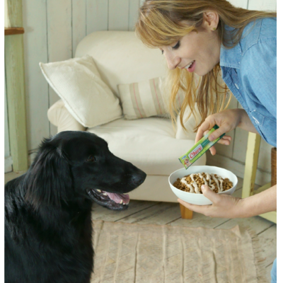 Mulher a dar comida a um cão preto com saco verde Cesar em casa