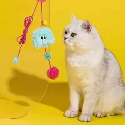 Brinquedo felpudo para gatos com bolas e flor suspenso perto de gato branco.