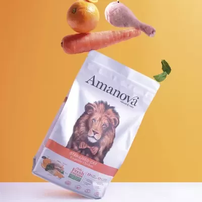 Pacote de ração para gato Amanova com imagens de leão e ingredientes, cenoura, laranja e asa de frango ao fundo.