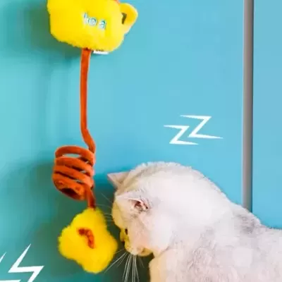 Brinquedo para gatos amarelo e castanho com bule e flor, gato branco ao lado em fundo azul