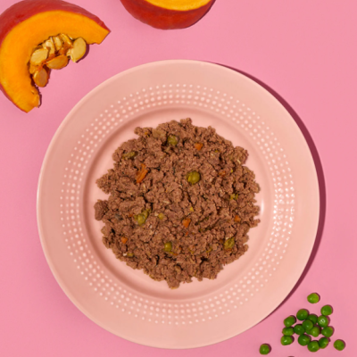 Prato rosado com carne moída e ervilhas, fatias de abóbora e ervilhas soltas em fundo rosa.