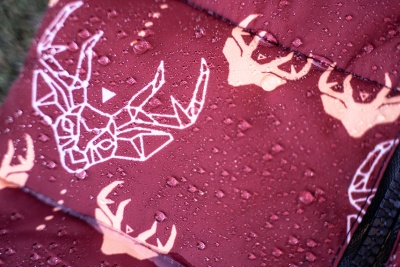 tecido impermeável vermelho escuro com padrão de veados geométricos e gotas de água