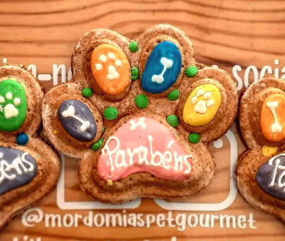 Biscoito em forma de pata decorado com glacê colorido e texto 'Parabéns'