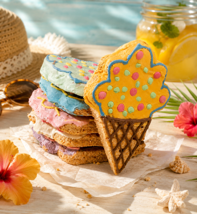 Biscoitos coloridos em forma de gelado empilhados numa mesa com decoração de verão