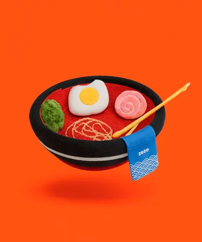 Valor decorativo de tigela com fios coloridos simulando comida, pauzinhos e etiqueta 'zeze' sobre fundo laranja