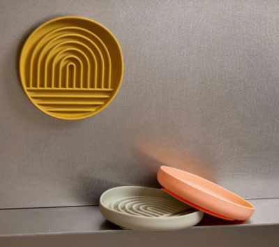 Três pratos redondos de silicone com relevo tipo arco-íris em amarelo, cinza e laranja