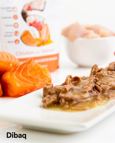 Refeição húmida para animais com carne em molho, pedaços de salmão e embalagem com texto Chicken with Salmon e marca Dibaq.
