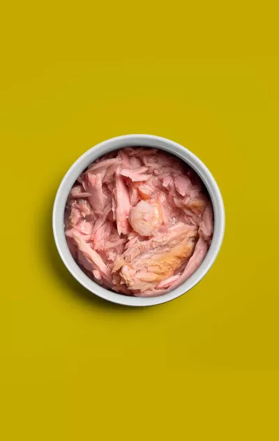 Taça branca com atum em pedaços rosa claro sobre fundo amarelo