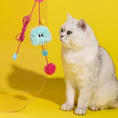 Brinquedo felpudo para gatos com bolas e flor suspenso perto de gato branco.