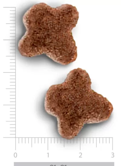 Dois pedaços de ração castanho escuro em forma de cruz arredondada sobre régua graduada