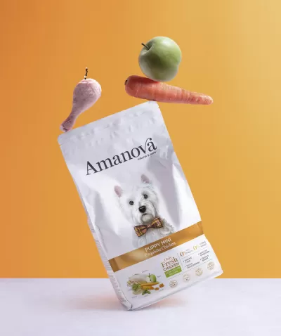Embalagem de ração Amanova Puppy Mini com cenoura, maçã verde e coxa de frango flutuando diante de fundo laranja