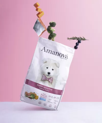 Saco branco de ração para cães Amanova Puppy Sensitive com imagem de cachorro e elementos flutuantes