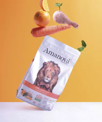 Pacote de ração para gato Amanova com imagens de leão e ingredientes, cenoura, laranja e asa de frango ao fundo.