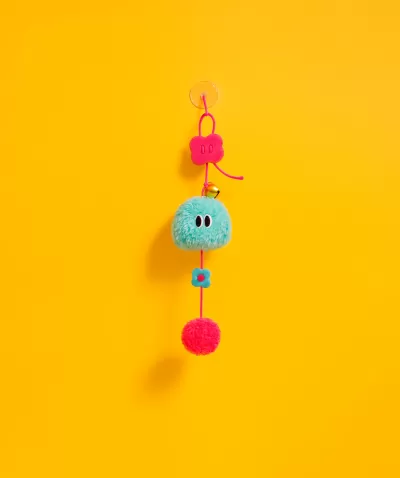 Chaveiro colorido pendurado com pompom azul, flores rosa e pompom vermelho num fundo amarelo