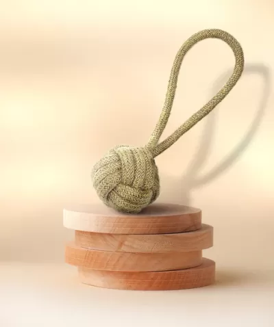 Nó de corda verde sobre pilha de discos de madeira clara num fundo bege