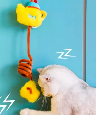 Brinquedo para gatos amarelo e castanho com bule e flor, gato branco ao lado em fundo azul