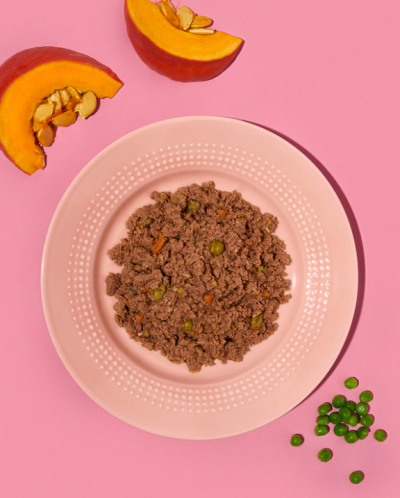 Prato rosado com carne moída e ervilhas, fatias de abóbora e ervilhas soltas em fundo rosa.