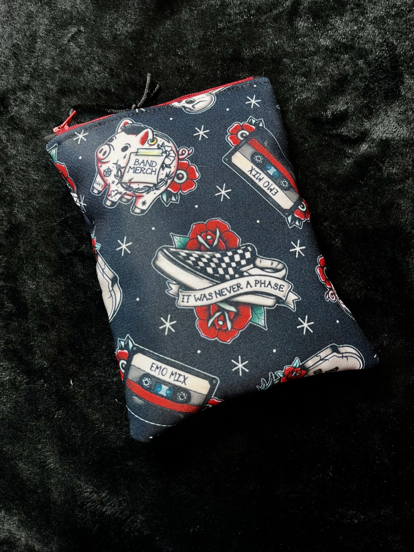 Elder Emo E-Reader Fabric pouch with tattoo-style patterns including pig, BAND MERCH text, EMO MIX cassettes, checkered sneakers, and red roses on black background.