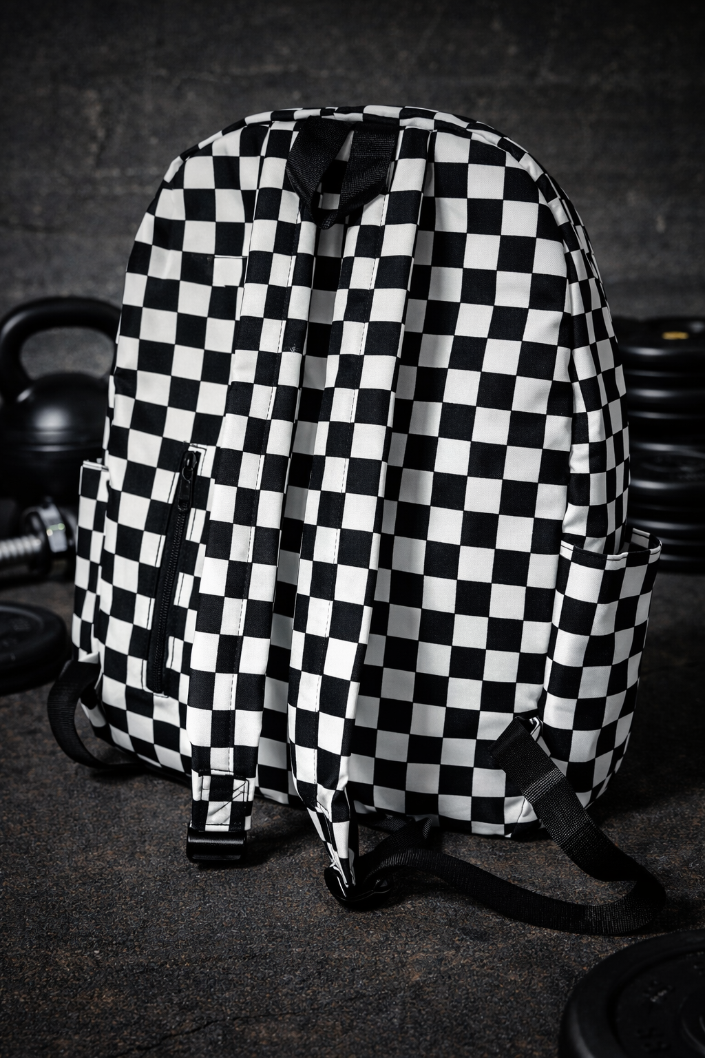 Gym Backpack - Pit Checker Black and white checkered backpack with straps on a gym floor