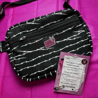Black crossbody bag with white barbed wire pattern and MOSHPIT MEMORIES patch on purple background with card