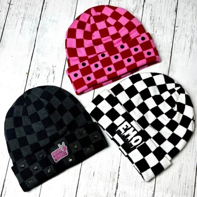 Three checkerboard patterned beanie hats in black/grey, pink/red, and black/white on white wooden floor