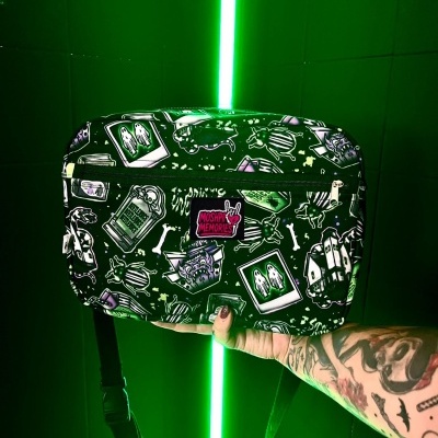 Black Halloween-themed crossbody bag with MOSHPIT MEMORIES patch held by tattooed arm