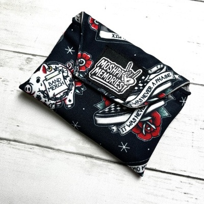 Folded black fabric pouch with band merch and Mosphit Memories print on white wood background