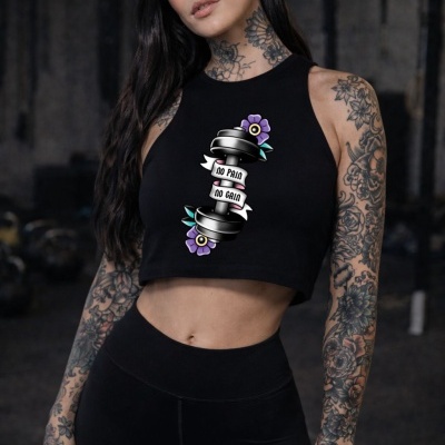 Woman wearing black sleeveless crop top with dumbbell graphic and tattooed arms in gym