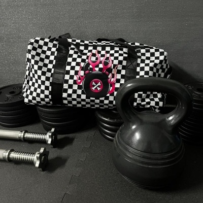 Black and white checkered duffel bag with pink flame logo next to gym weights and kettlebell