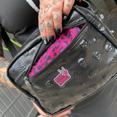 Black leather bag with skull embossing, MOSHPIT MEMORIES patch, and pink leopard print lining visible inside zipped pocket.