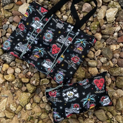 Black tote bag and pouch with colorful tattoo designs and text on rocky ground
