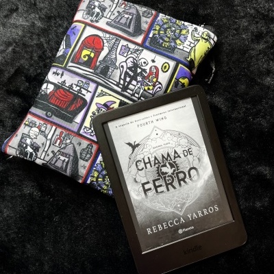 Kindle e-reader with CHAMA DE FERRO book cover and colorful cartoon fabric pouch on black fur background