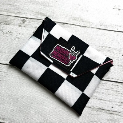Black and white checkered pouch with MOSHPIT MEMORIES pink label on white wood background