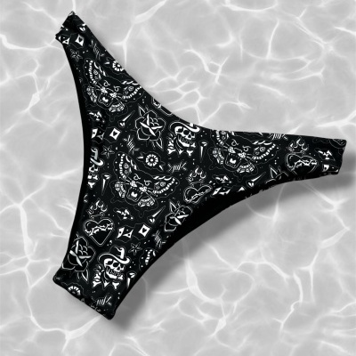 Black bikini bottom with white tattoo-inspired print on light grey water background