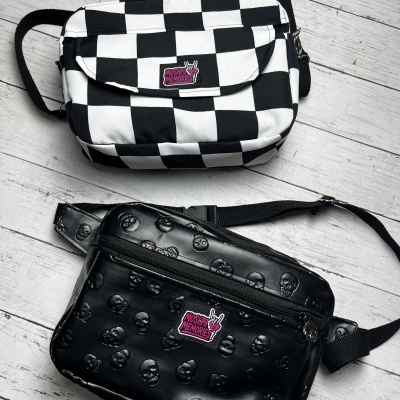 Two crossbody bags, one black and white checkerboard patterned and one black with embossed skulls, both with MOSH PIT MEMORIES labels.