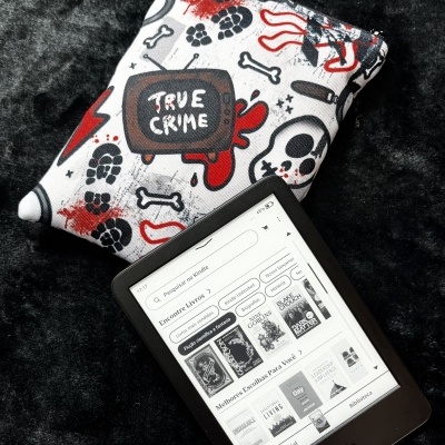 Amazon Kindle e-reader with book store interface and a True Crime themed fabric pouch on black surface