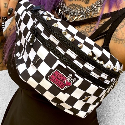 Black and white checkered fanny pack with spikes and MOSHPIT MEMORIES patch worn by person with tattoos and purple hair.