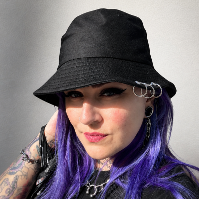 Mulher com chapéu bucket preto com argolas metálicas e cabelo roxo