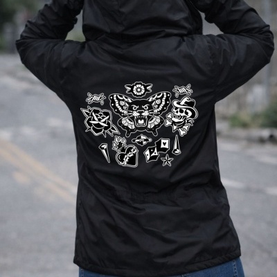 Black jacket with white tattoo-style graphics on back worn by person standing outdoors