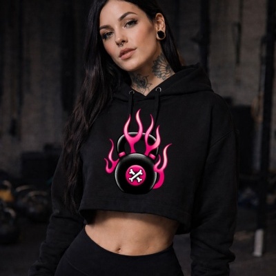 Black cropped hoodie with pink flaming kettlebell graphic worn by tattooed woman in gym