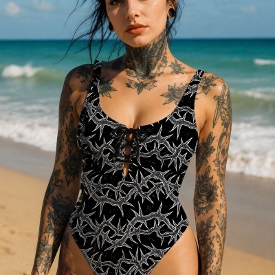 Tattooed woman wearing black and white patterned one-piece swimsuit on a beach