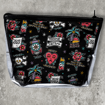 Black toiletry bag with colorful tattoo-style prints and various texts on a concrete surface