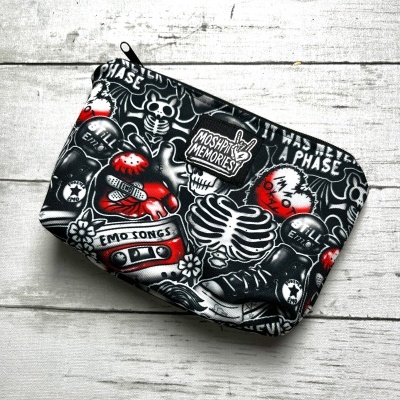 Black pouch with skeleton and skull designs and multiple white and red text on a white wooden surface