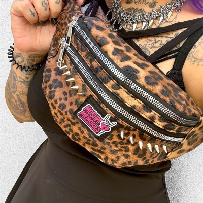 Leopard print fanny pack with spikes and zippers held by tattooed person with purple hair