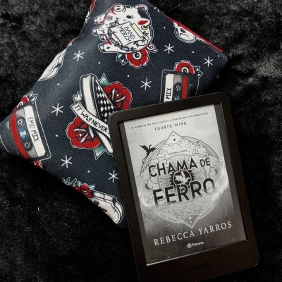 Kindle e-reader displaying book cover Chama de Ferro by Rebecca Yarros next to a fabric pouch with dark blue background and colorful prints