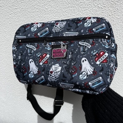 Black shoulder bag with colorful tattoo-style prints and multiple text patches against white wall.