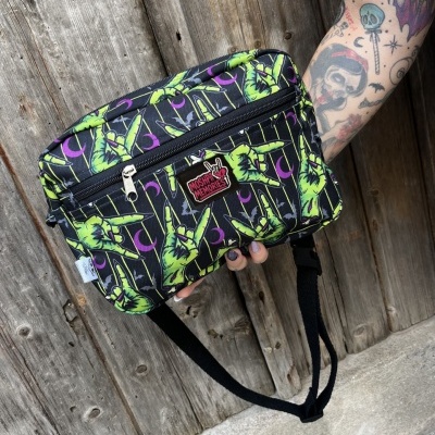 Black waist bag with green zombie hands and purple moons pattern, MOSH PIT MEMORIES patch, held by tattooed arm