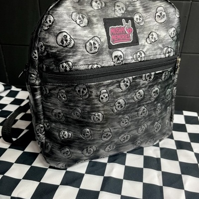 Black skull-patterned backpack with MOSHPIT MEMORIES patch on black and white checkered surface