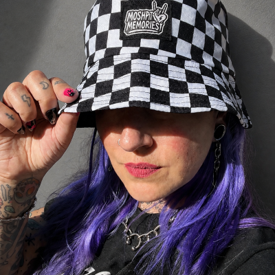 Black and white checkered bucket hat with MOSHPIT MEMORIES patch worn by person with purple hair and tattoos